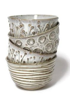 four white bowls stacked on top of each other in different sizes and shapes, all decorated with silver swirls