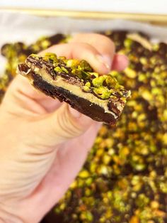 a hand holding up a piece of chocolate and pistachio covered cookie bar in front of the camera