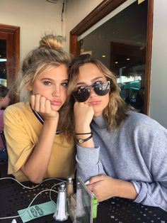 two young women sitting at a table with their hands on their chins and looking into the camera