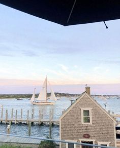 a sailboat is out on the water near a house and dock at sunset or dawn