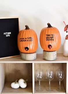 two pumpkins sitting on top of a wooden shelf next to wine glasses and a chalkboard