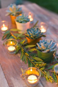 candles and succulents are lined up on a wooden table with greenery