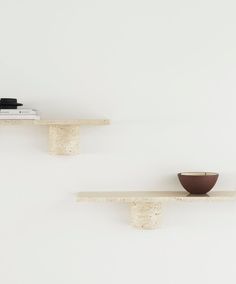 two wooden shelves with bowls on them against a white wall, one shelf has a book and the other is a bowl