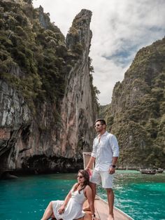 a man and woman on a boat in the water near some cliffs with blue water