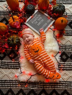 a baby laying on top of a white rug next to oranges and pumpkins