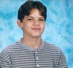 a young boy wearing a striped shirt and posing for a photo in front of a blue background