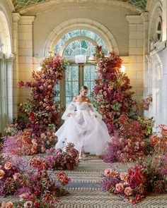 a woman in a white wedding dress standing on steps surrounded by flowers