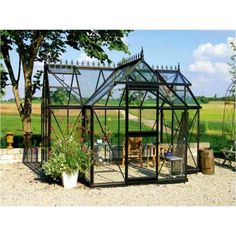 a small glass house sitting in the middle of a gravel field next to a tree