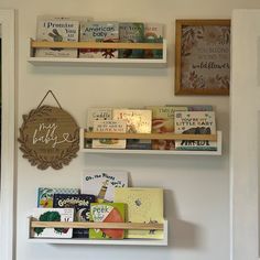 three wooden shelves with books on them and a sign hanging from the wall behind them