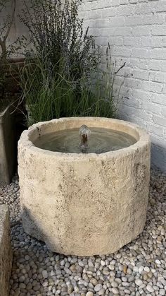 there is a water fountain in the middle of some rocks and gravel next to a brick wall