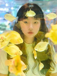 a young woman is surrounded by yellow flowers and fish in front of the glass window