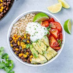 a bowl filled with rice, beans, avocado and other vegetables next to lime wedges