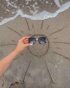 a person is holding sunglasses in the sand at the beach and drawing a heart on the sand