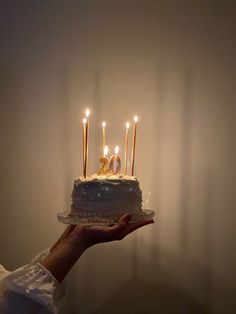 a person holding a cake with candles on it in front of a white wall that says 20