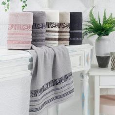 towels are lined up on a towel rack next to a potted plant in a white room