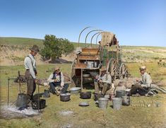 three men are sitting in the grass with buckets and pots on their laps while another man stands near them