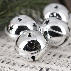 three silver bells with stars on them sitting on top of music sheets next to a christmas tree