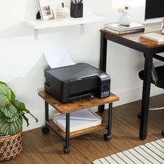 a printer sitting on top of a wooden table next to a potted green plant