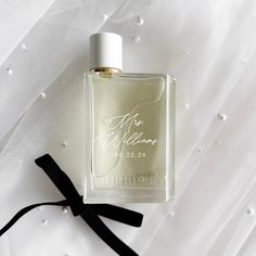 a bottle of perfume sitting on top of a white bed sheet next to a black ribbon