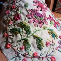 a white hat with pink flowers and green leaves embroidered on the front, sitting on a wooden table