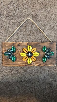 a wooden sign with green and yellow flowers hanging from it's side on a wall