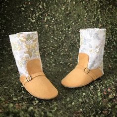 two pairs of baby shoes sitting on top of green grass with flowers and leaves in the background