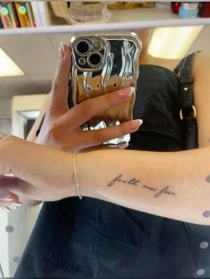 a woman holding a cell phone in her right hand and writing on the back of her left arm