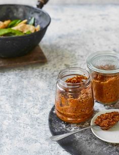 two jars filled with food sitting on top of a table next to a bowl and spoon