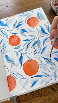 someone is painting an orange on a piece of paper with watercolors and brush