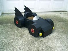 a homemade batman car made out of toilet paper on the sidewalk with garage doors in the background