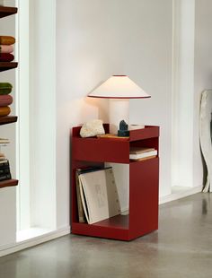 a red book shelf with a lamp on top and books in the bottom corner next to it