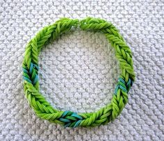 a green and blue braided bracelet sitting on top of a white blanket