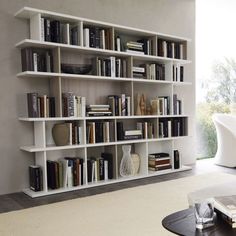 a living room filled with lots of white furniture and bookshelves next to a window