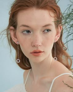 a woman with red hair wearing earrings and a white top is looking at the camera