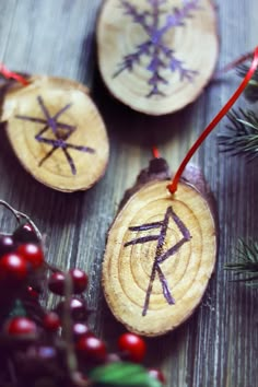 three wooden ornaments with symbols on them are hanging from red string and surrounded by berries