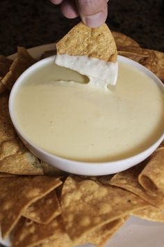 a person dipping cheese into a bowl of dip surrounded by tortilla chips on a plate