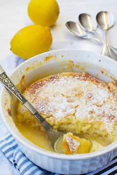 a bowl of lemon cobbler with a spoon in it and two lemons next to it