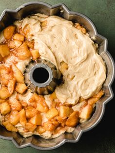 a bundt cake with apples and cream frosting in a pan on a table