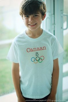 a young boy standing in front of a window wearing a shirt with the olympic rings on it