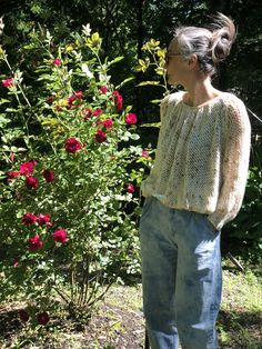 a woman standing in front of a bush with red flowers on it's side