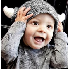 a young boy wearing a knitted hat and holding his hands up to his head