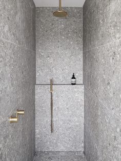 a walk in shower sitting next to a tiled wall and floor with gold fixtures on it