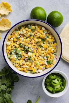 a bowl filled with corn next to tortilla chips and limes