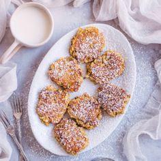 powdered sugar covered pastries on a white plate next to a cup of milk