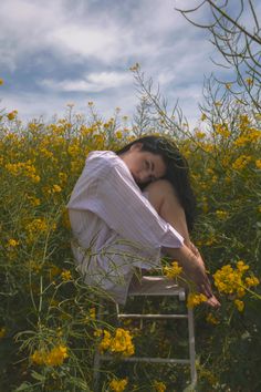 a woman sitting on top of a wooden chair in a field of yellow wildflowers