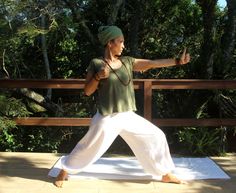 a woman in white pants and a green shirt is doing yoga on a wooden deck