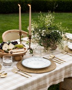 a table set with plates, silverware and candles on top of it in the grass