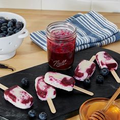 blueberry cheesecake pops are on a black cutting board next to a bowl of blueberries