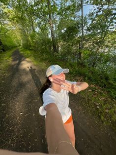 a woman is taking a selfie while walking down a dirt path in the woods