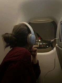 a woman sitting in an airplane with headphones on and looking at the television screen